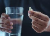man holding a pill in one hand and glass of water in another