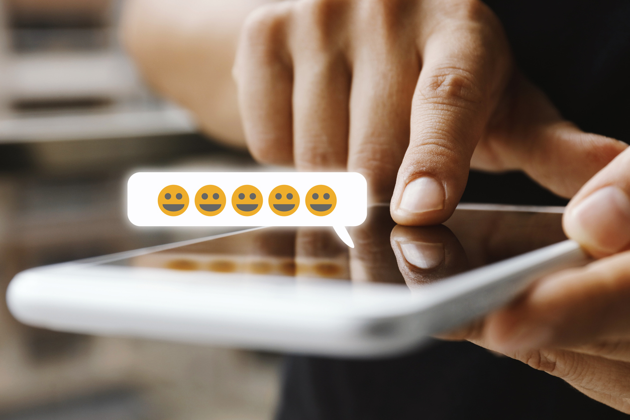 A person's hands use a smartphone to add smiling emojis to a message.
