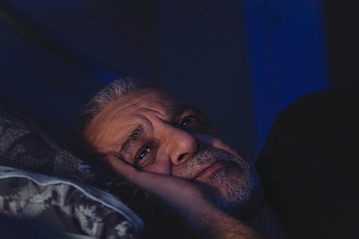 Elderly man can't sleep, lays awake in bed with eyes open, looking deep in thought