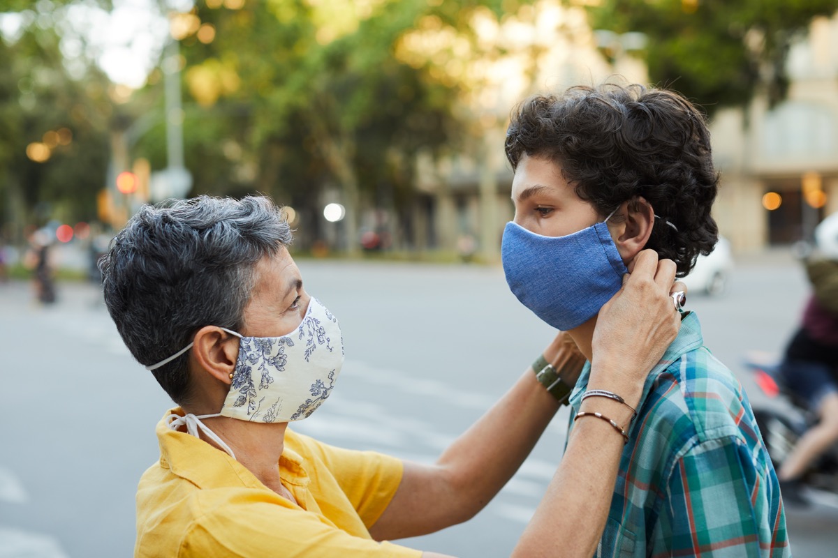 A caring mother is adjusting her teenager son's COVID mask