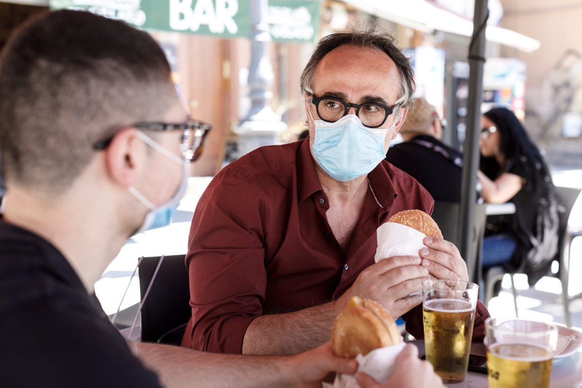 two men wearing masks while eating outdoors