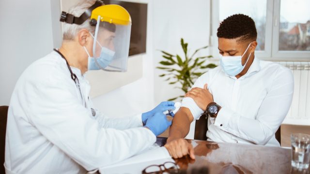 Senior male doctor vaccinates a young man in a doctor's office
