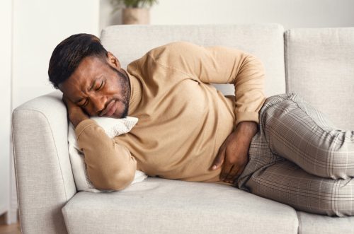 Man Touching Aching Stomach Lying On Couch At Home