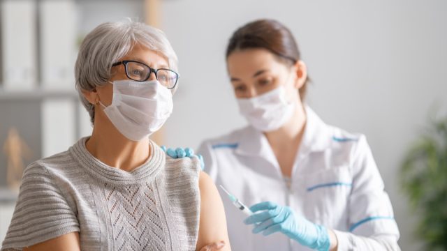 gray haired woman getting a covid vaccine from young female doctor