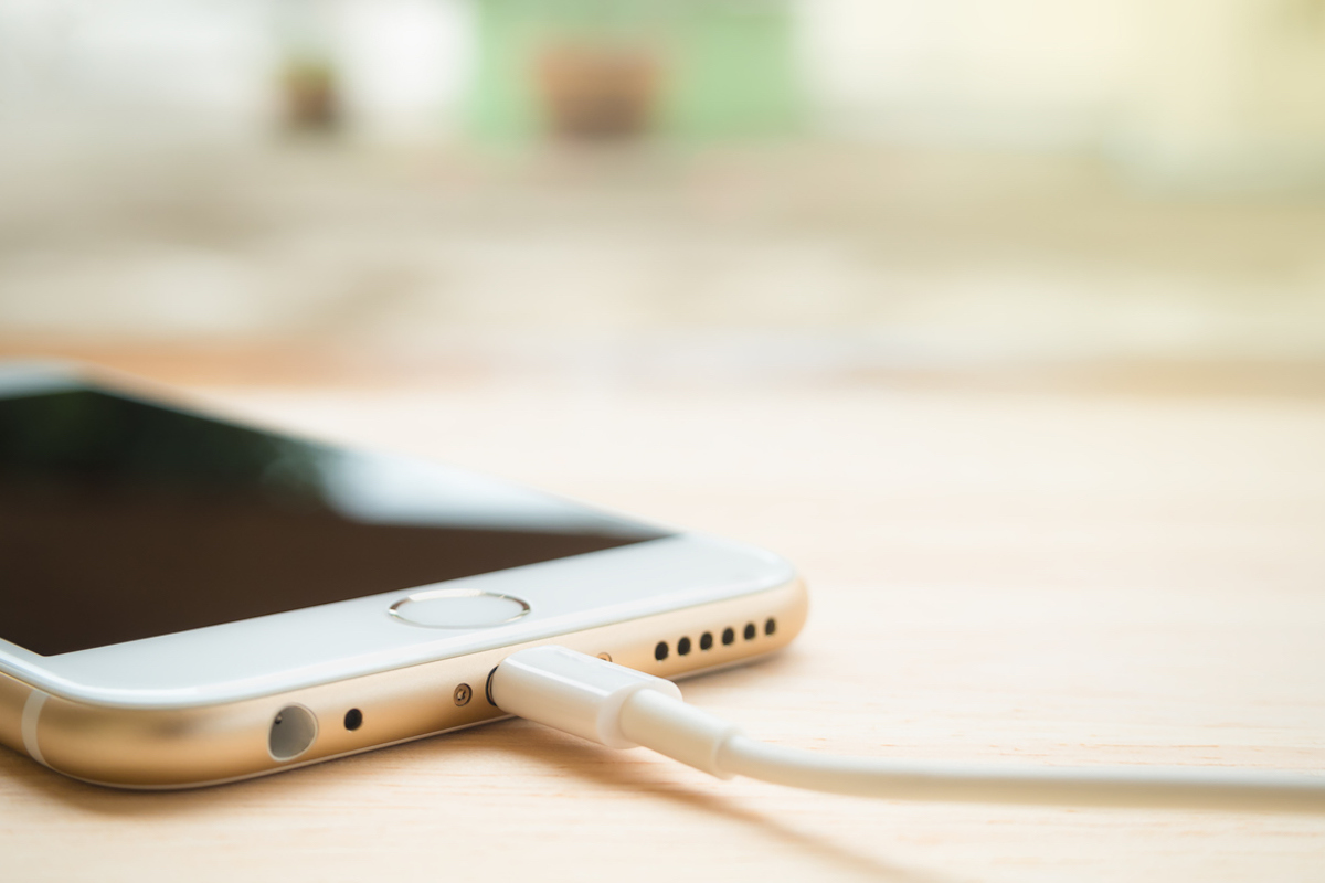 Close-up image of the Apple iPhone 6S charging with Lightning USB cable on the wooden table