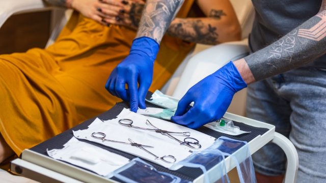 piercer in piercing studio wearing blue gloves and touching implements on tray