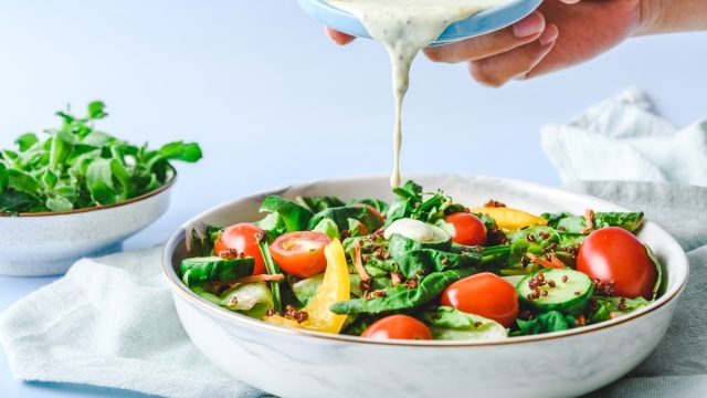 hand pouring a cream-based salad dressing onto a salad in a white bowl