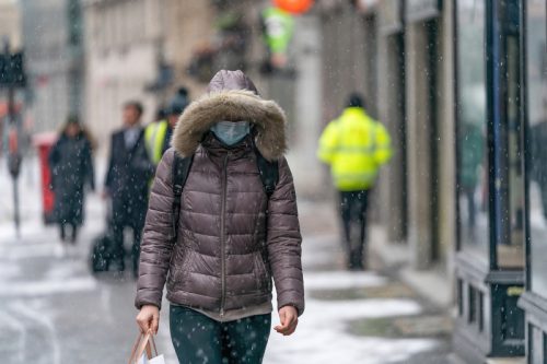 woman in winter clothing and face mask walking in snow