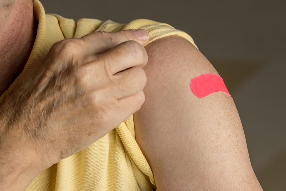 Senior man holding up shirt sleeve to show the sticking plaster after a flu jab in shoulder