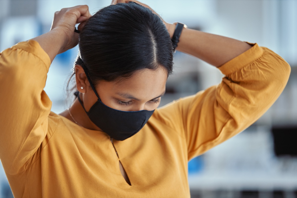 Shot of a young woman putting on a mask in a modern office
