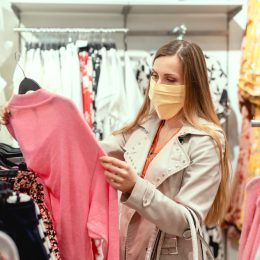 A young woman wearing a face mask picks up a shirt while shopping in a department store.