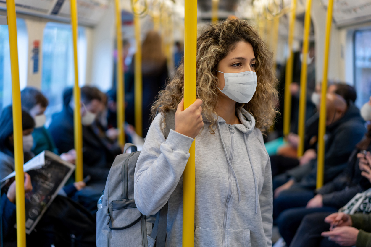 A young woman wearing a face mask riding on public transportation.