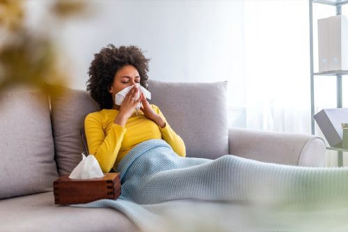 young woman in yellow sweater blowing nose on couch