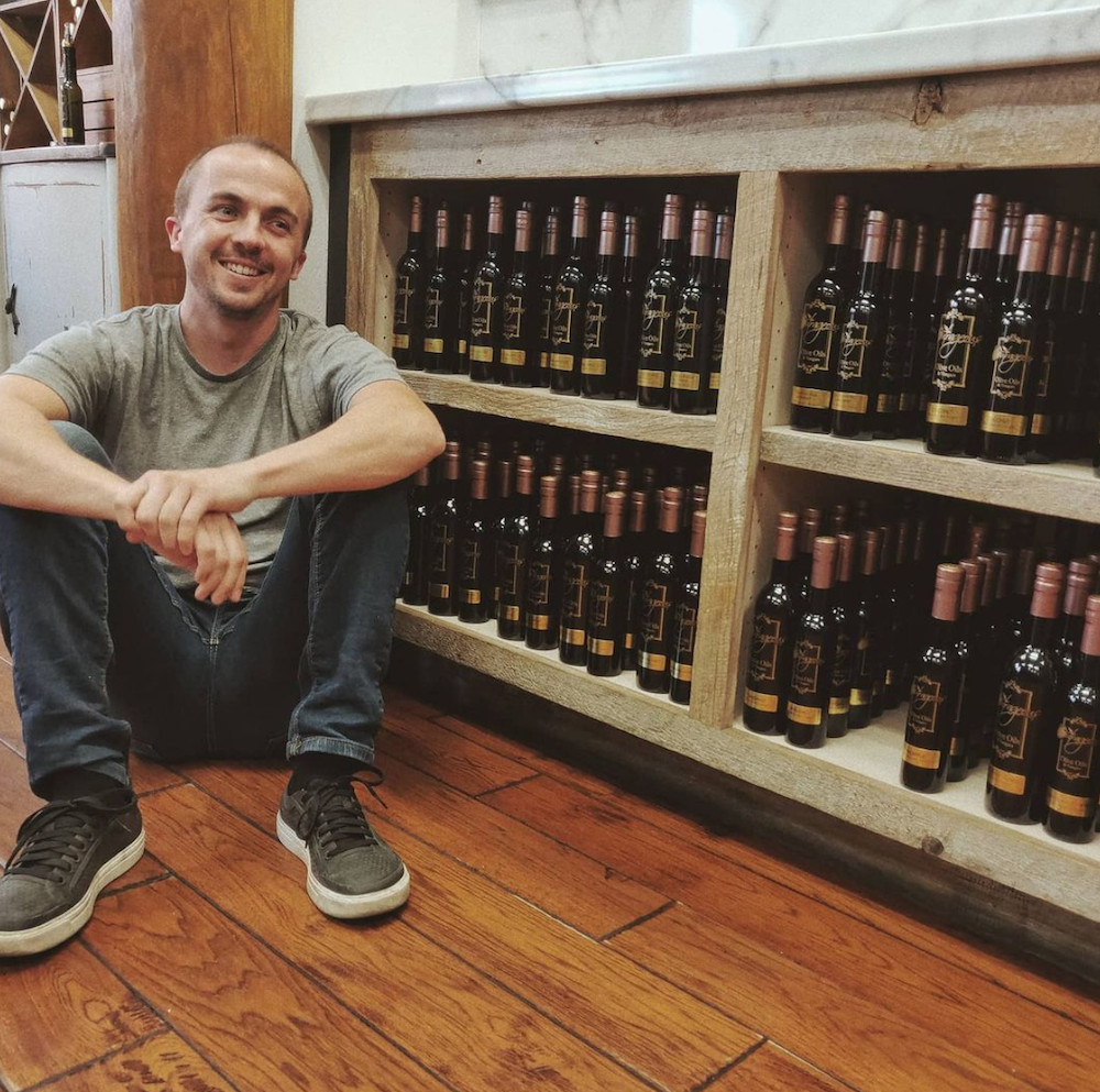 Frankie Muniz posing near bottles of olive oil in the shop he owned