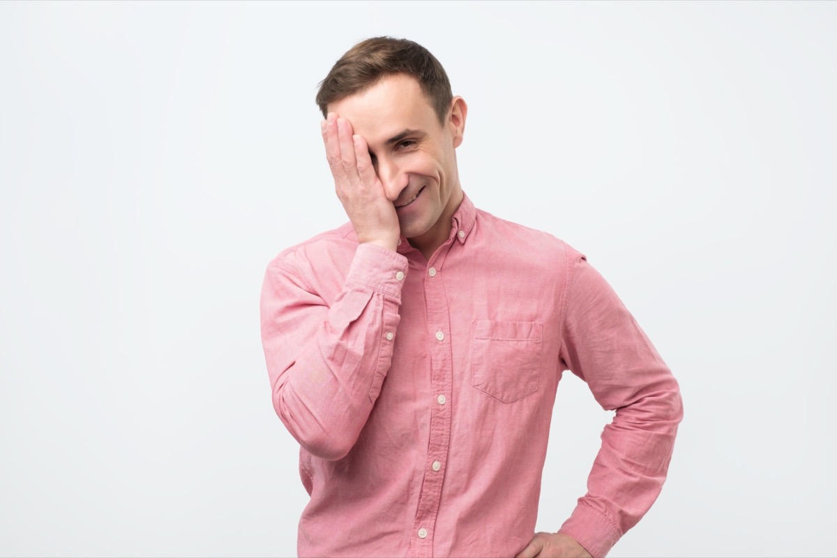 Man in pink shirt against white background trying not to laugh