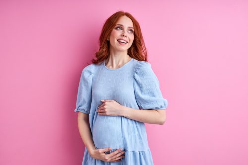 Rothaarige schwangere Frau in einem blauen Kleid