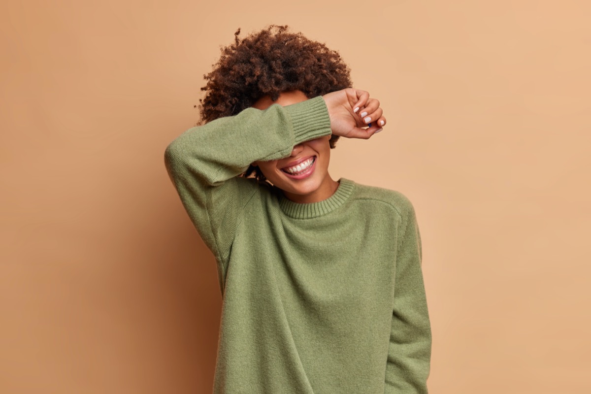Woman in green sweater covering eyes with her arm and laughing