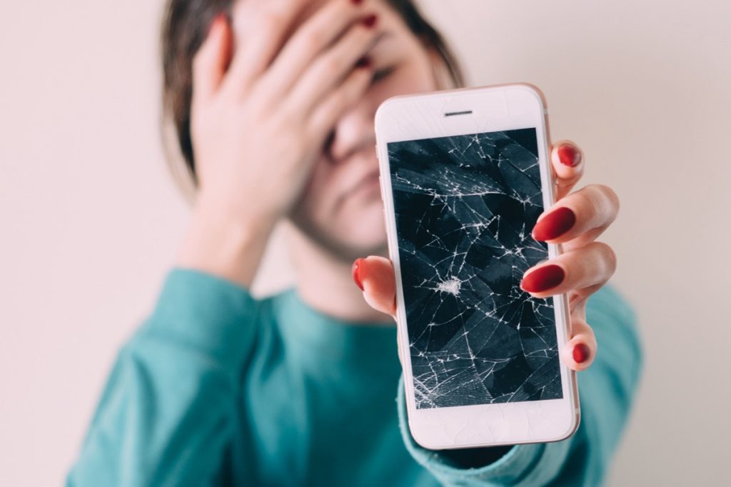 Woman holding out phone with cracked screen
