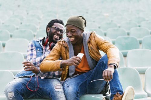 Two young male friends sitting in empty stadium seats laughing