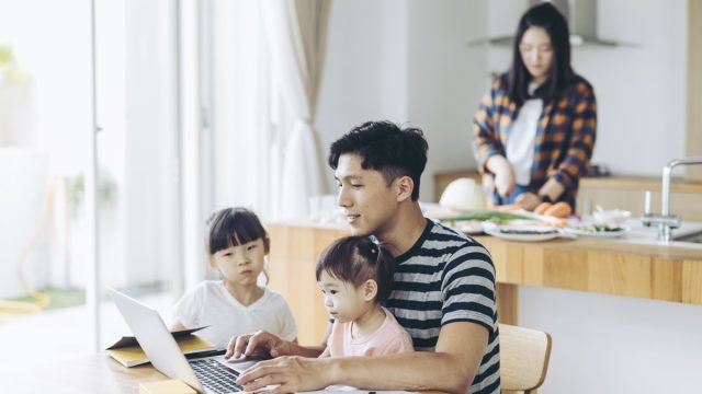 Father with two children using laptop to work from the living room.