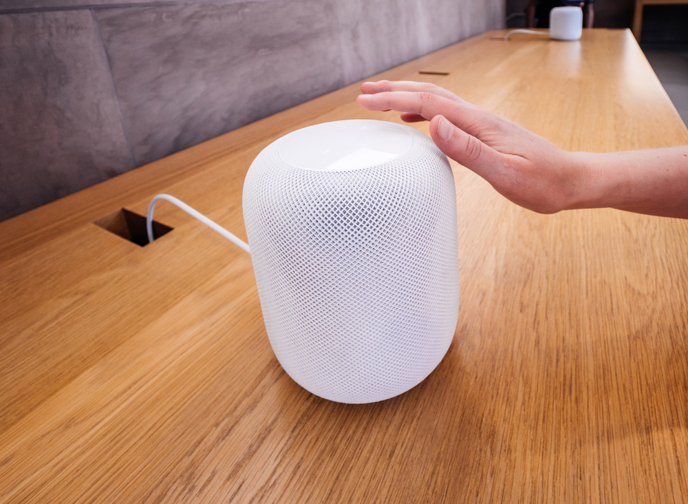 A hand activates a white Apple HomePod that is being displayed in the Apple Store.