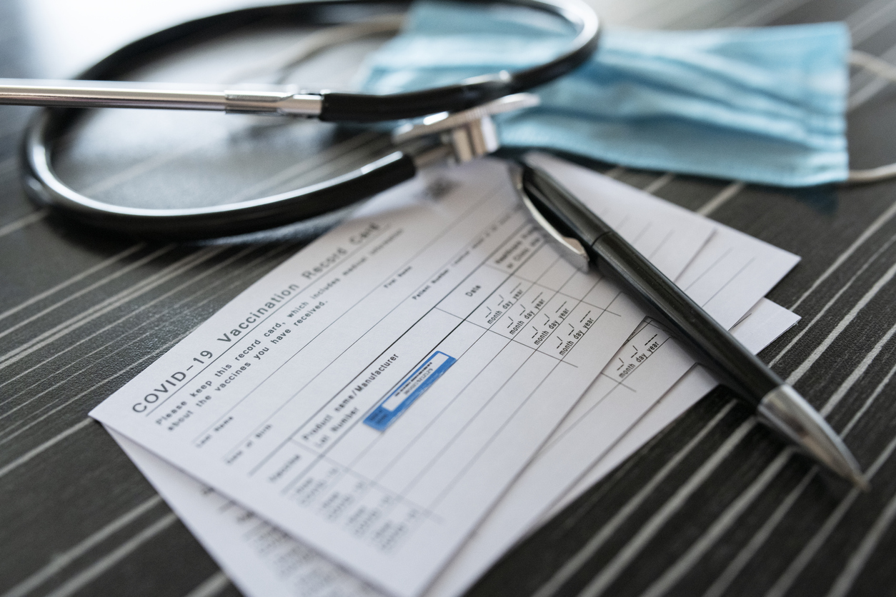 A COVID-19 vaccination record card sitting on a table next to a face mask and stethoscope