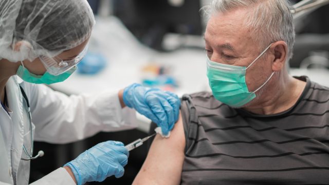 A doctor gives an injection in the shoulder with the COVID vaccine to an elderly male patient