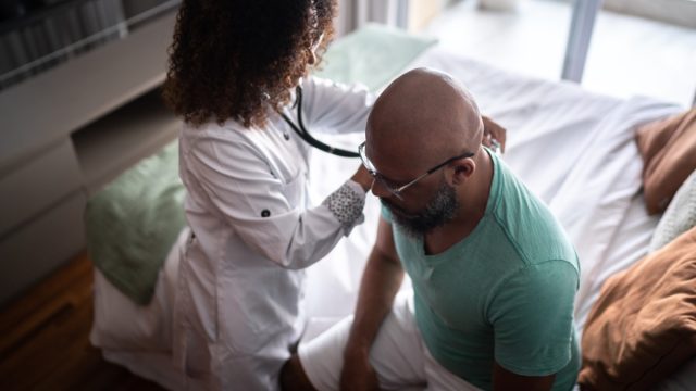 Doctor listening to patient's heartbeat during home visit