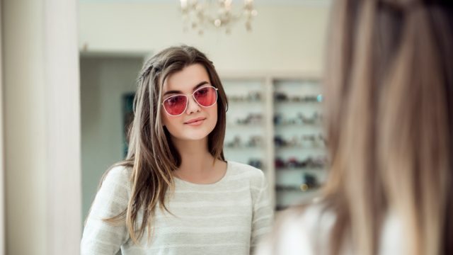 young woman with brown hair trying on sunglasses