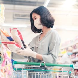 woman wearing face mask and rubber glove in supermarket looking at snacks