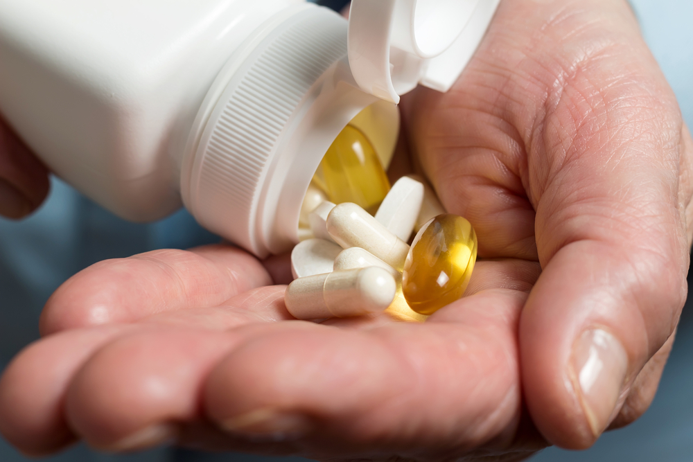 A hand holding various dietary supplement pills coming out of a bottle.