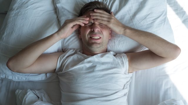 Man lying in bed at home suffering from headache or hangover