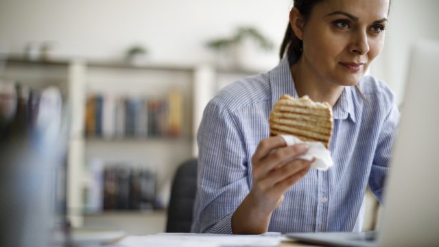 Woman working from home and eating a sandwich for lunch at her laptop