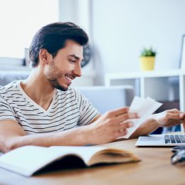 A young man filing taxes on his laptop while smiling and maybe cashing his COVID stimulus check