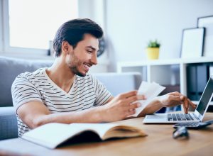 A young man filing taxes on his laptop while smiling and maybe cashing his COVID stimulus check