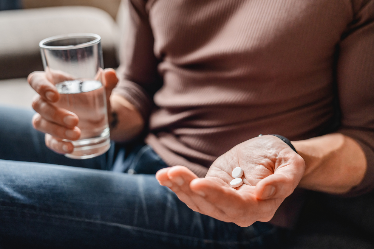 A person holding two pills in the palm of his hand and a glass of water