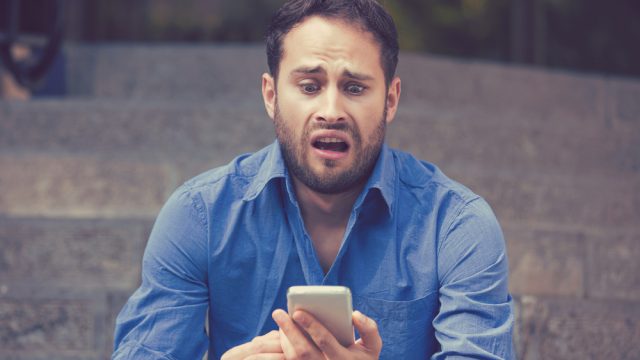 A young man looking at his smartphone with a horrified look on his face.