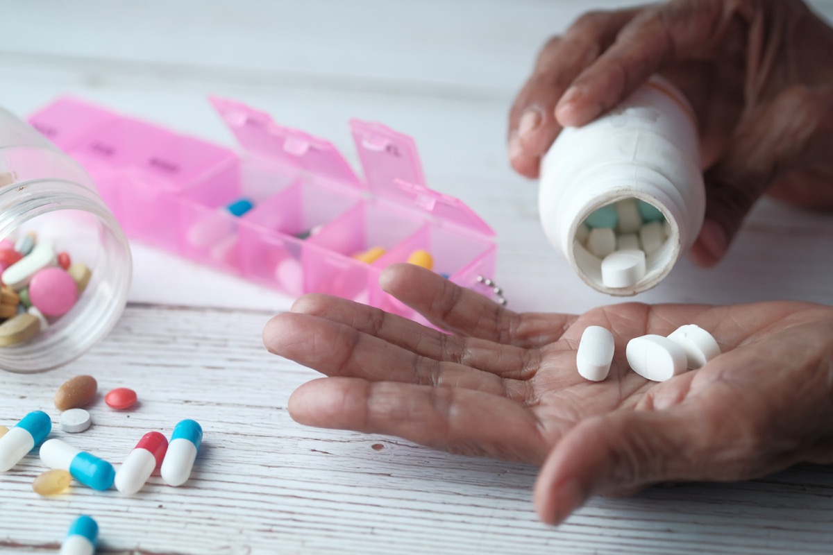 Elderly woman pouring pills from bottle on hand, close up view