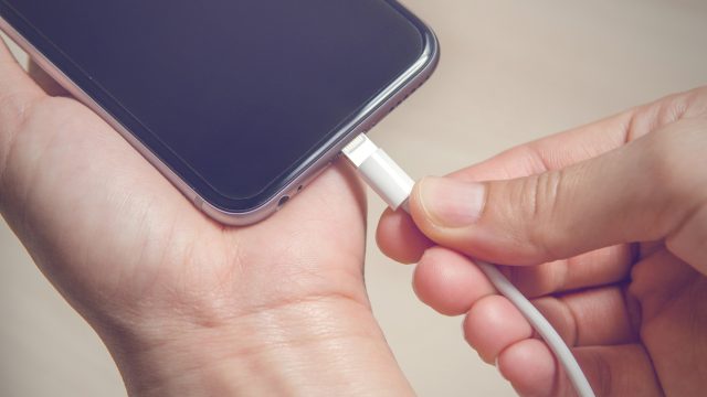 Hands plugging in an iPhone charger into its base