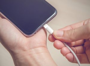 Hands plugging in an iPhone charger into its base