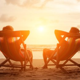 Silhouette of happy young retired couple sitting in deck chairs on the beach at sunset