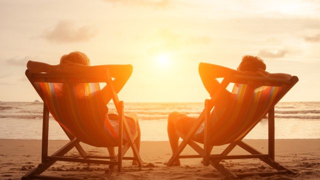 Silhouette of happy young retired couple sitting in deck chairs on the beach at sunset