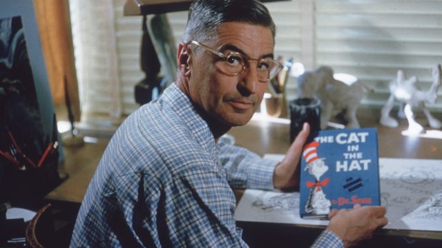 American author and illustrator Dr Seuss (Theodor Seuss Geisel, 1904 - 1991) sits at his drafting table in his home office with a copy of his book, 'The Cat in the Hat', La Jolla, California, April 25, 1957. (Photo by Gene Lester/Getty Images)