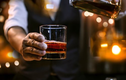 Bărbat ținând whisky bourbon într-un pahar transparent