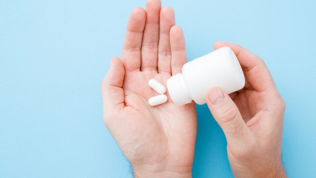 Man spilling out white pills from bottle in his hand.