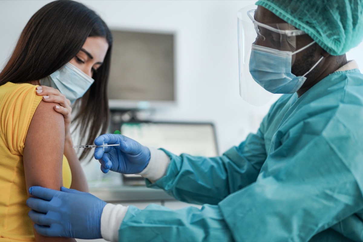 woman getting vaccine from doctor in face shield and scrubs