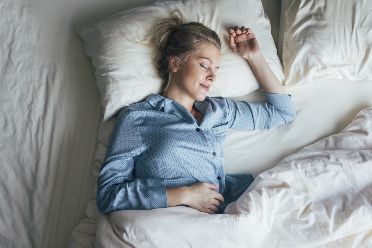woman in blue pyjamas sleeping on a king-size bed.