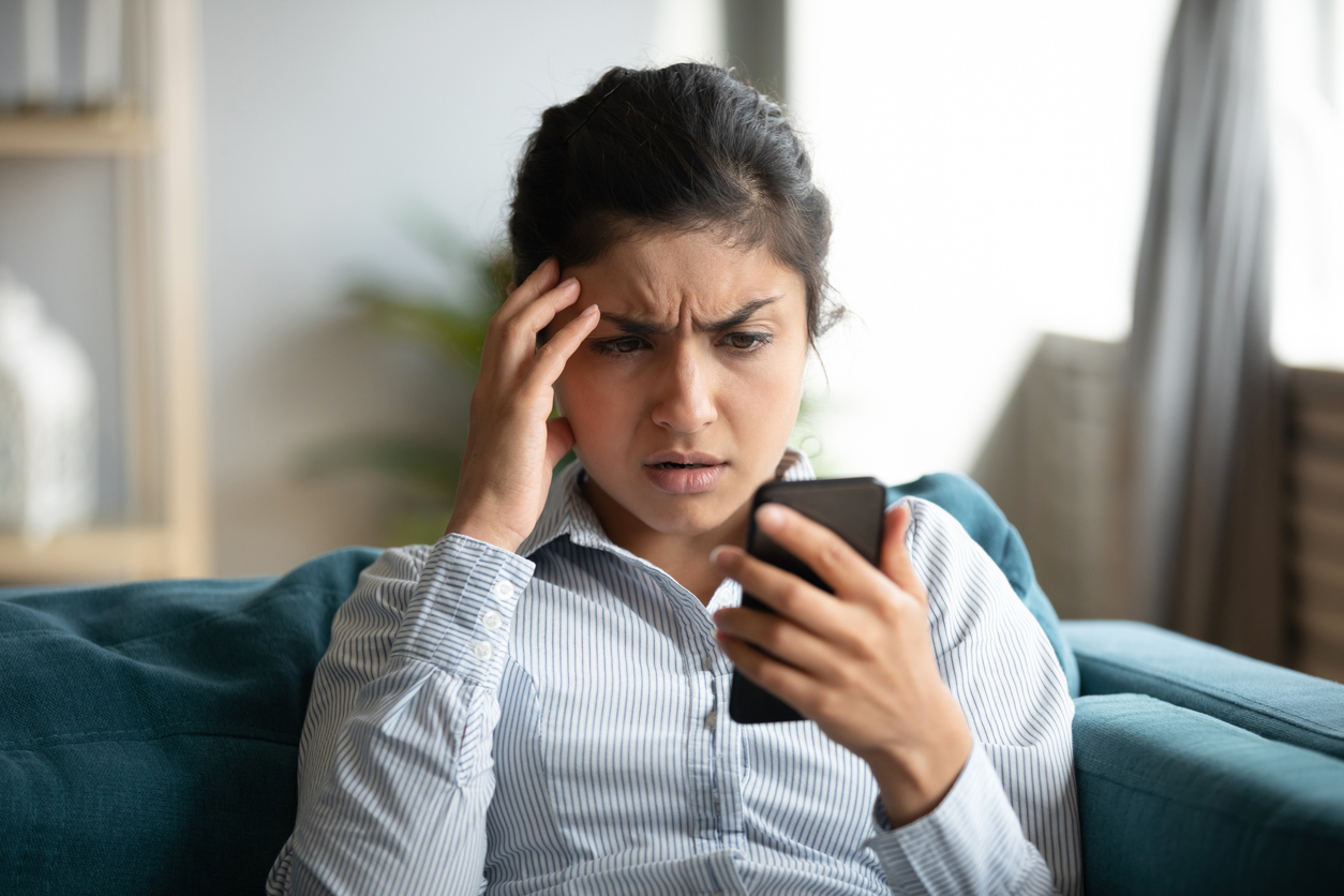 Млада жена гледа у свој паметни телефон са забринутим изразом на лицу.