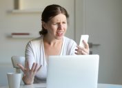 A young woman looks angrily at her cell phone while reading a text message