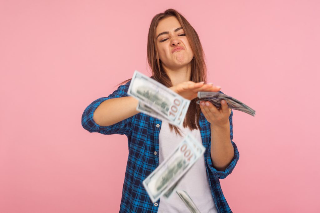 Woman standing against pink background, making it rain hundred dollar bills